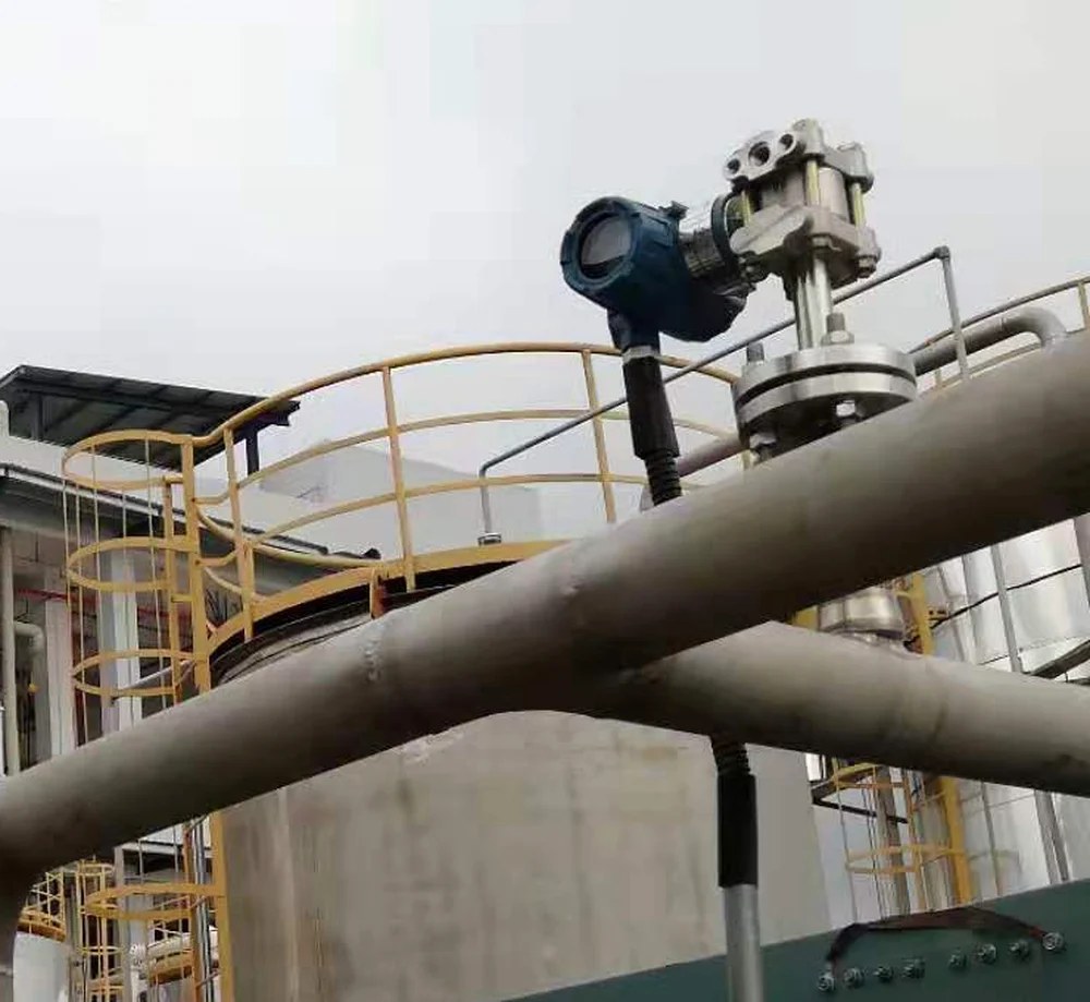 Pressure transmitter installed on a flanged tank nozzle at an outdoor process plant with guard railing and stainless piping