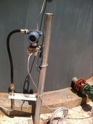 Pressure transmitter installed outdoors at the base of a storage tank, exposed to weather, with field cabling