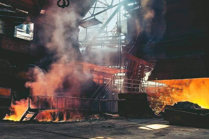 Working blast furnace cast house with smoke and glowing hot metal during tapping