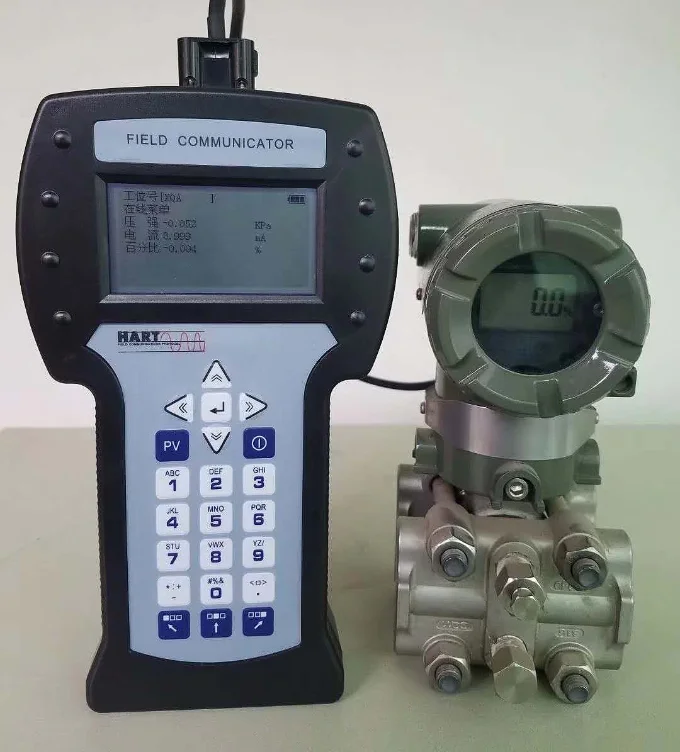 Handheld HART field communicator connected to a differential pressure transmitter, its screen showing the tag, pressure and loop current