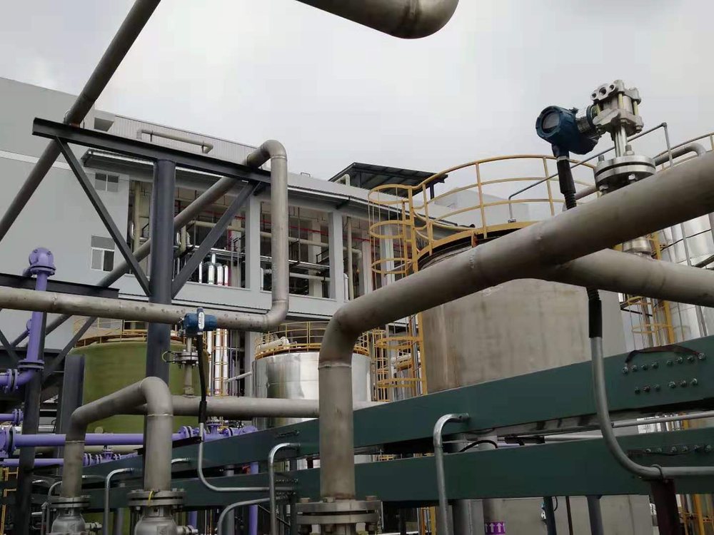 Flange-mounted level transmitter on a vertical storage tank nozzle in an outdoor plant, with process piping and access platforms around the tank