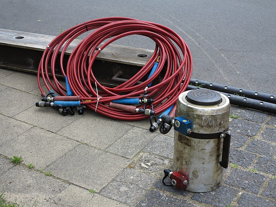 Hydraulic lifting cylinder on a paved yard with coiled red high pressure supply hoses