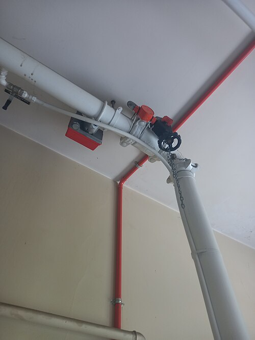 Sprinkler riser near a ceiling with a red waterflow switch box and a control valve on the white pipe